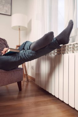 Soğuk bir kış günü, kitap okurken, evde ısıtan radyatörde çoraplı bir adamın ayakları..