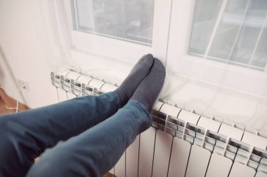 Soğuk bir kış gününde evin ısıtıcı kaloriferinde çoraplı bir adamın ayakları..