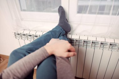 Soğuk bir kış gününde evin ısıtıcı kaloriferinde çoraplı bir adamın ayakları..