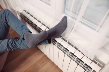 Soğuk bir kış gününde evin ısıtıcı kaloriferinde çoraplı bir adamın ayakları..