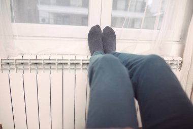 Soğuk bir kış gününde evin ısıtıcı kaloriferinde çoraplı bir adamın ayakları..