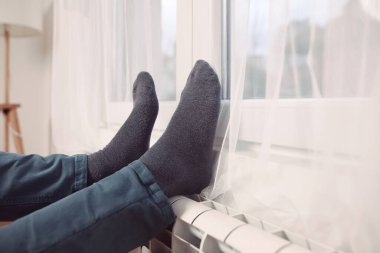 Soğuk bir kış gününde evin ısıtıcı kaloriferinde çoraplı bir adamın ayakları..