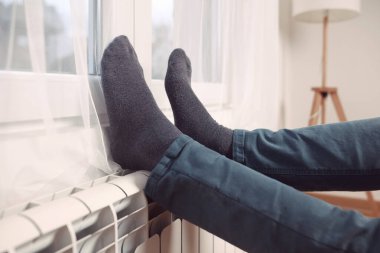 Soğuk bir kış gününde evin ısıtıcı kaloriferinde çoraplı bir adamın ayakları..