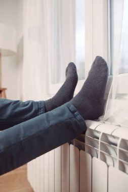 Soğuk bir kış gününde evin ısıtıcı kaloriferinde çoraplı bir adamın ayakları..