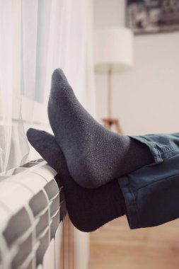 Soğuk bir kış gününde evin ısıtıcı kaloriferinde çoraplı bir adamın ayakları..