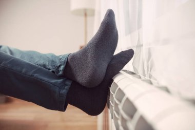 Soğuk bir kış gününde evin ısıtıcı kaloriferinde çoraplı bir adamın ayakları..