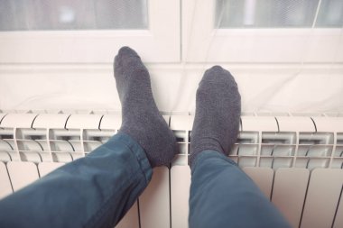 Soğuk bir kış gününde evin ısıtıcı kaloriferinde çoraplı bir adamın ayakları..