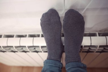 Soğuk bir kış gününde evin ısıtıcı kaloriferinde çoraplı bir adamın ayakları..