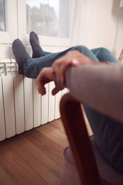 Soğuk bir kış gününde evin ısıtıcı kaloriferinde çoraplı bir adamın ayakları..