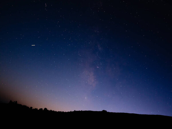 Milky way stars and constellations with landscape silhouettes photographed from a dark countryside location.