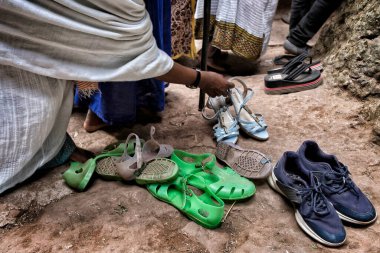 Lalibela, Ethiopia - January 7, 2018: A woman picking her shoes out of a church in Lalibela. During the first days of January, thousands of Ethiopian Orthodox Christian pilgrims go to the city of Lalibela in Ethiopia. clipart