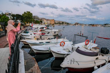 Sinop, Turkey - July 31, 2024: A woman taking photos of the boats moored in the port of Sinop, Turkey. clipart