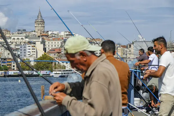 İstanbul, Türkiye - 20 Eylül 2024: İstanbul, Türkiye 'de Galata Köprüsü' nde arka planda Galata Kulesi ile balık tutan insanlar.