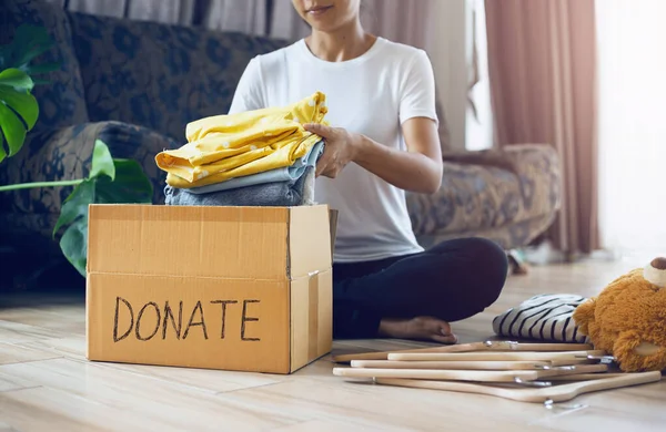 stock image Woman holding Clothes with Donate Box In her room, Donation Concept.