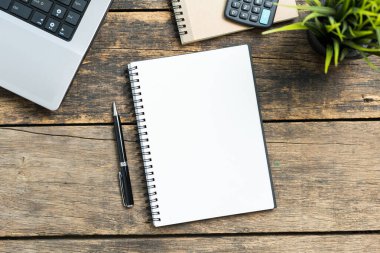 Akıllı telefonu ve bilgisayarı ahşap masa üstünde olan boş bir defter.