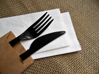 Plastik siyah çatal ve bıçak beyaz bir peçete üzerinde kaba kumaştan bir arka plana karşı
