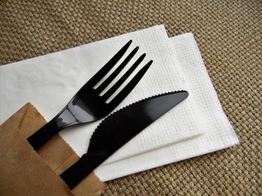 Plastik siyah çatal ve bıçak beyaz bir peçete üzerinde kaba kumaştan bir arka plana karşı