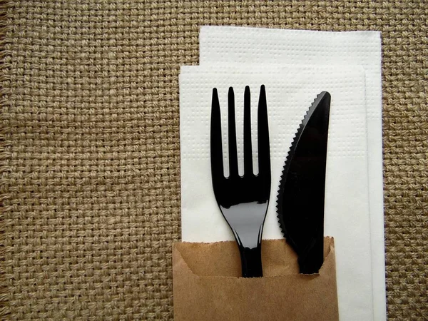 白色餐巾上的塑料黑色叉子和小刀 与粗糙织物衬托在一起 — 图库照片