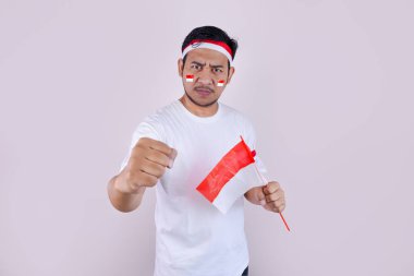Beyaz tişörtlü ve Endonezya bayraklı Asyalı bir adam Endonezya Bağımsızlık Günü kutlamalarında poz veriyor. Fotoğraf vatanseverliği ve ulusal gururu yansıtıyor..