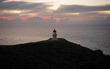 Günbatımında Aupouri Yarımadası Northland Kuzey Adası Yeni Zelanda 'da okyanus kıyısındaki kayalıklarda duran tarihi beyaz Cape Reinga deniz feneri manzarası