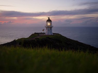 Günbatımında Aupouri Yarımadası Northland Kuzey Adası Yeni Zelanda 'da okyanus kıyısındaki kayalıklarda duran tarihi beyaz Cape Reinga deniz feneri manzarası