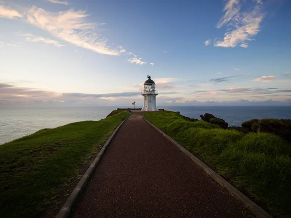 Pedestrian asphalt road walkway leading to historic white lighthouse landmark perched on oceanside clifftop Cape Reinga Aupouri Peninsula Northland North Island New Zealand