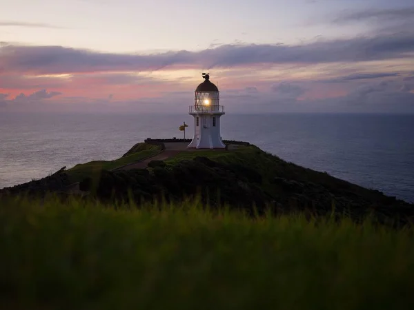 Panoramic view of historic white Cape Reinga lighthouse landmark perched on oceanside clifftop during sunset in Aupouri Peninsula Northland North Island New Zealand