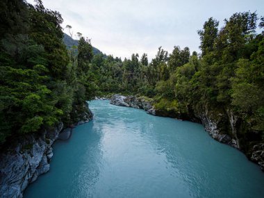Turkuaz mavi buzul nehir suyu beyaz granit kaya uçurumları kanyonundan Hokitika Gorge Kokatahi Batı Yakası Yeni Zelanda 'da yemyeşil ağaç ormanıyla doluyor.