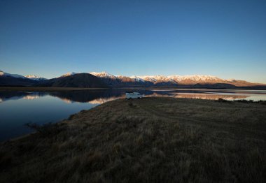 Beyaz karavanlı karavan karavanı Heron Gölü 'nün uzak kırsalında kamp kuruyor kış günbatımı, Ashburton Lakes Canterbury Güney Adası Yeni Zelanda' daki Güney Alpler dağları.