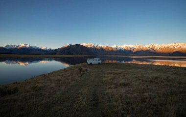 Beyaz karavanlı karavan karavanı Heron Gölü 'nün uzak kırsalında kamp kuruyor kış günbatımı, Ashburton Lakes Canterbury Güney Adası Yeni Zelanda' daki Güney Alpler dağları.