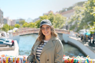 Portekiz 'in Aveiro şehrinde güneşli bir günde, bir köprüde poz veren güneş gözlüklü güzel bir genç kadın..