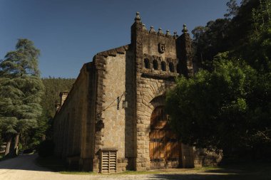 Toprak yolun dibindeki sarmaşıklarla kaplı taştan evin yatay görüntüsü. Tamber nehrinin çevresinde güneşli bir bahar günü. Noia, A Coruna, Galiçya.