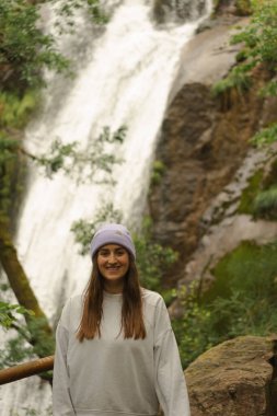 Gülümseyen bir kadın Porto do Son 'da sisli bir yürüyüş sırasında yakalanan Ribasieira şelalesinin önünde duruyor. Şelalenin ve etrafındaki ormanın doğal güzelliği....