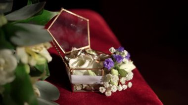 Two gold engagement rings in a glass box and a branch with white and blue flowers and leaves on the red surface. Engagement rings, copy space