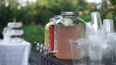 Limonata, cam kavanozda dilimlenmiş taze limon ve açık hava ahşap masa musluğu. Cam kavanozlarda üç farklı ev yapımı limonata ve şenlik masasında tıkırtı. Yaz partisi