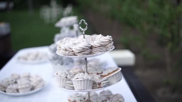 お祝いのテーブルには 3層のケーキとマカロンで飾られたカラフルな白いテーブルクロスが覆われています 結婚式のコンセプトのお祝い 白い結婚式の高級キャンディーバー — ストック動画