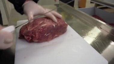 A Butcher Cuts fresh Beef Meat with a sharp fillet Knife on a white cutting board. Meat Shop Production Line. Close up