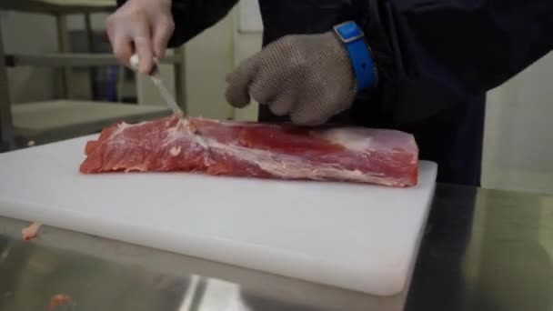 屠夫手戴着金属防护手套的特写镜头 在切白木板上的猪肉片上切下工人刀 — 图库视频影像