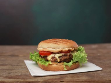 Big Burger ahşap masaya karşı beyaz kağıt üzerinde uzanıyor. Meyveli yeşil salata yaprağı ve hamburgerin yanında kırmızı domates.