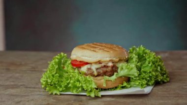 Lezzetli bir Burger Ahşap Masa 'nın üzerinde yeşil bir arka planda yatıyor.