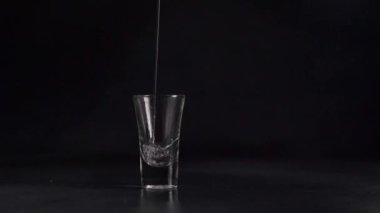Bir su akıntısı, siyah bir zemine karşı bir bardağa doluyor. Su sıçraması. Yavaş çekim. 120fps