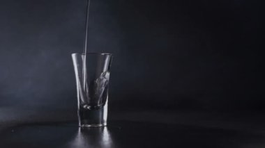 Bir su akıntısı, gri bir zemine karşı bir bardağa doluyor. Su sıçraması. Kapat.