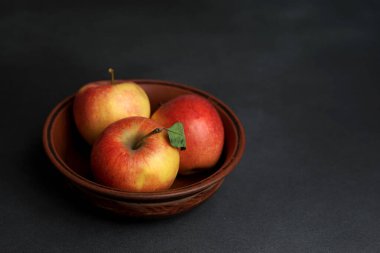 Üç kırmızı sulu elma, siyah bir zemine karşı bir kil tabakta yatar. Boşluğu kopyala