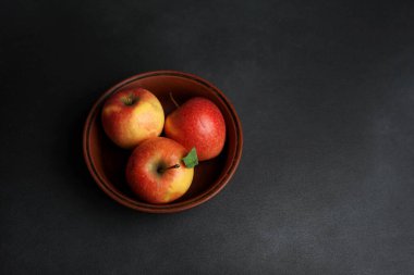 Üç kırmızı sulu elma, siyah bir zemine karşı bir kil tabakta yatar. Boşluğu kopyala