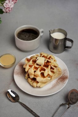 Lezzetli waffle tabağı, karamel sosu, kahve fincanı, gri arkaplanda süt.