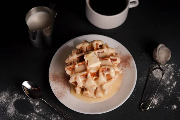 stock image Homemade of tasty Belgian Waffles Plate, Caramel Sauce, Coffee Cup, Milk on a Black concrete Background