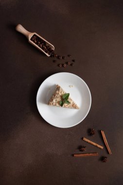 Lezzetli Napolyon Pastası 'nın üst görüntüsü. Kahverengi bir arka planda naneli şeker filizi ile süslenmiş beyaz bir tabakta krema. Tarçın çubuğu, badyan, kahverengi arkaplanda kahve çekirdekleri. Boşluğu kopyala