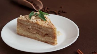 Lezzetli Napolyon Pastası 'nı kapayın. Kahverengi arka planda bir tutam nane ile süslenmiş beyaz bir tabağa krema koyun. Tarçın çubuğu, badyan, kahverengi arkaplanda kahve çekirdekleri. Boşluğu kopyala
