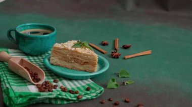 Yeşil arka planda bir tutam nane ile dekore edilmiş turkuaz bir tabakta kremalı nefis Napolyon keki. Bir fincan sıcak kahve, tarçın çubuğu, badyan, yeşil arkaplanda kahve çekirdekleri.
