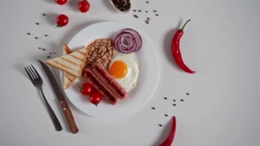 İngiliz Kahvaltısı. Kızarmış yumurta, iki kızarmış sosis, kızarmış ekmek tostu, konserve fasulye, mavi soğan ve beyaz arka planda vişneli domates. Genel Görünüm